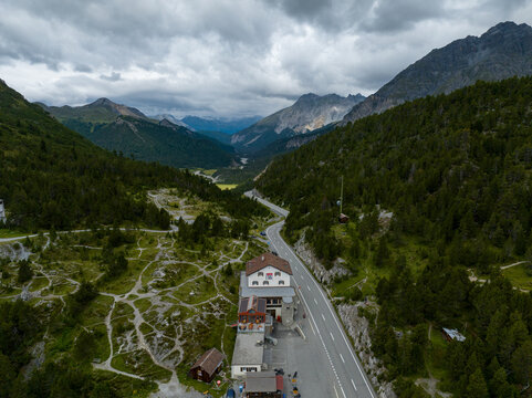 Aerial view of Fuorn Pass featuring a winding mountain road through dense pine forests and rugged peaks Val Mustair, Grisons, Switzerland.