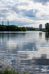 Obraz premium Clear reflections on a calm lake surface with clouds and urban landscape in the background during the daytime