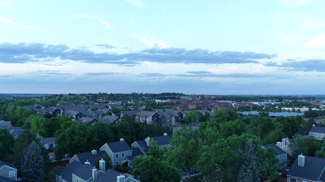 Aerial of suburban residential neighborhood in Denver Colorado at dusk with mature trees houses and roads visible under a cloudy evening sky