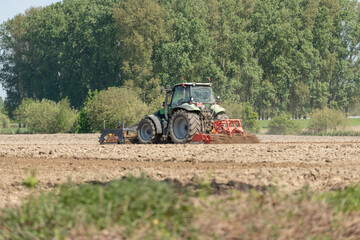 Obraz premium Diepenbeek, Belgium. Tractor cultivating farmland with soil preparation machinery during active fieldwork in rural landscape