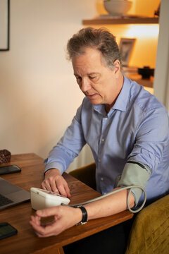 Mature man measuring blood pressure at home using digital monitor