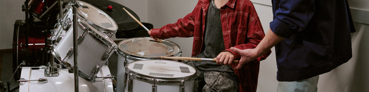 Website banner of teenager playing drum kit while adult instructor guiding hand position during music lesson, supporting skill development and arts education marketing
