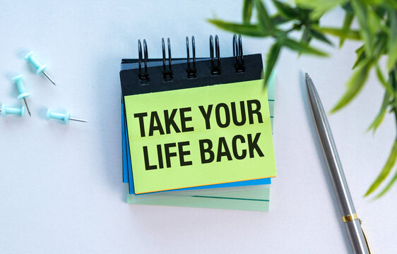 Bright yellow sticky note says Take Your Life Back. Black spiral notebook rests on light blue sheets.