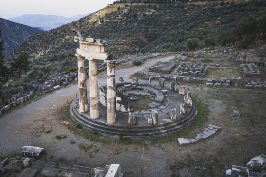 Aerial view of the ancient Tholos of Delphi at the Sanctuary of Athena Pronaia with its iconic circular structure and standing columns on a mountain slope in Delphi, Greece.