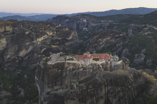 Aerial view of the Holy Monastery of Varlaam perched on a massive sandstone rock pillar surrounded by the dramatic landscape of rock formations and lush green valleys Trikala, Greece.