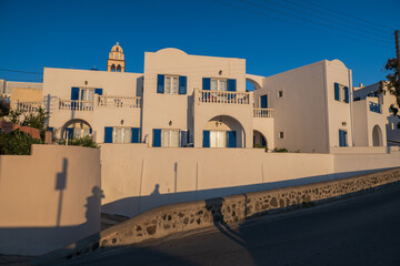 Sunlit Santorini street with traditional white buildings, blue windows, and church bell tower under clear summer sky. © Andrei Tomas