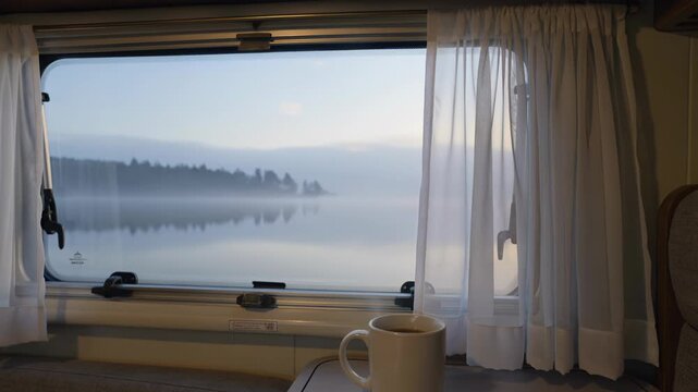 Morning coffee with a calm misty lake view from inside a camper van