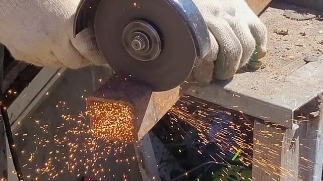 Male hand cuts off pieces of pipe with angle grinder. Cutting of a steel with splashes of sparks at construction site. Sparks during cutting of metal angle grinder