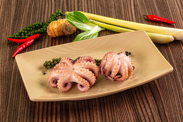 Cooked baby octopus dish with green peppercorns, red chili, lemongrass, and ginger on wooden table © Andrei Starostin