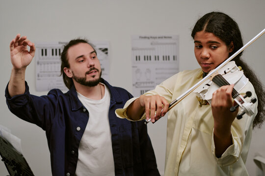 Teenager playing violin during lesson while male instructor guiding technique and rhythm. Useful for music education, private tutoring, arts training marketing
