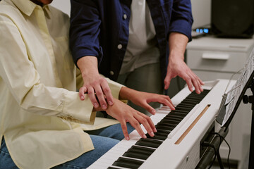 Teenager practicing piano with instructor guiding hand position on keyboard, showing music education and skill development. Useful for learning programs, tutoring services, close up shot © AnnaStills