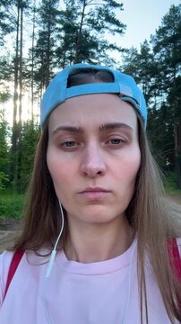 Close-up portrait of woman wearing blue backwards cap and headphones in pine forest, outdoor fitness and casual lifestyle concept