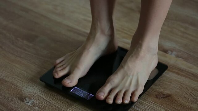Woman bare feet stepping on black digital floor scales, she weighing, checking herself at home on the floor. Measuring weight, control, wellness, diet body care concept