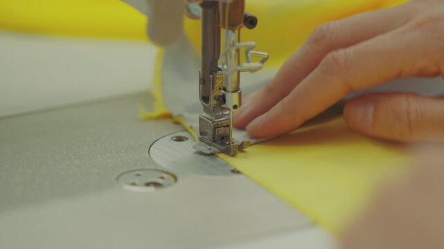 Close-up shot of a sewing machine needle stitching grey tape onto bright yellow fabric.