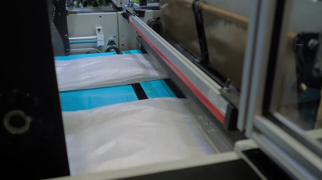 Automatic plastic bag making and cutting machine - production of packaging white bags at exhibition, factory: close up. Recycling, industry, manufacturing, and technology equipment concept