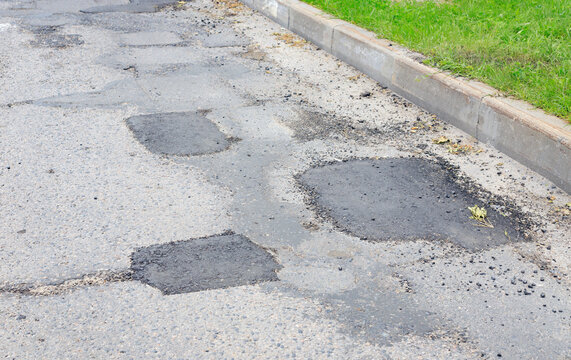 Asphalt road patching and pothole repair texture, grey street pavement surface with fresh dark bituminous layers close up