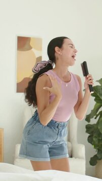 Vertical video: Singing woman in mauve top holding remote mic at home for pal with phone appearing