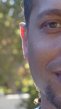 Vertical video: Blinking and smiling Hispanic man reacting to camera at park, with rim light bokeh