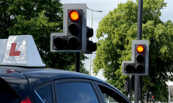 Learner driver car with L plate at red traffic light, driving school lesson, stop signal on city street, transport safety and learner permit education