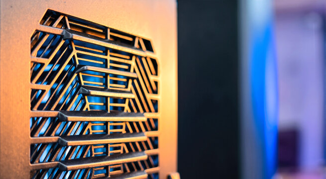 Close up of black ventilation louver with geometric pattern. Modern cooling system grille with warm orange light