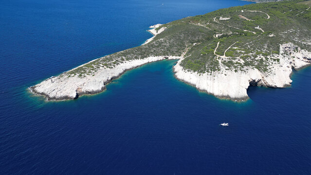 Aerial view of the rugged white cliffs and turquoise waters of the coastline on Vis island with a small boat in the deep blue sea Split-Dalmatia County, Croatia.