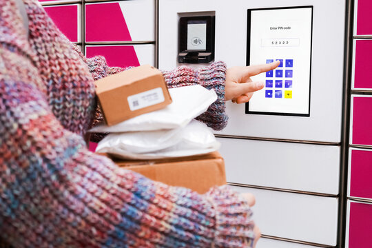 a woman uses an automated parcel locker terminal for an online shopping pickup, entering a code to receive a package from the delivery logistics service.