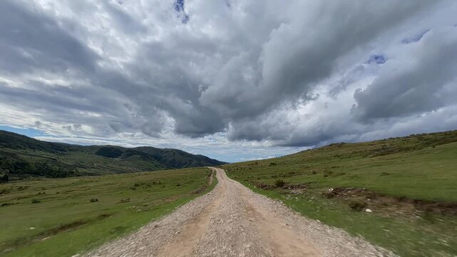 Scenic gravel path cutting through a vast rolling green highland under dramatic moving storm clouds