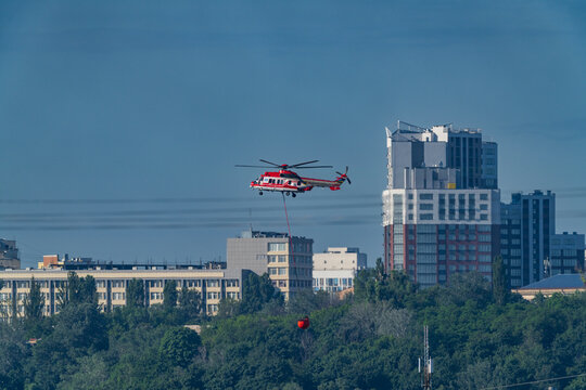 KYIV, UKRAINE &mdash; JUNE 15, 2026: Airbus H225 Super Puma firefighting helicopter of the State Emergency Service of Ukraine (SESU) carrying a water bucket to extinguish a massive fire over the city skylin