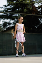 Naklejka premium Young girl prepares to play tennis on a court in summer with her racket focusing on her upcoming match against her friend or opponent