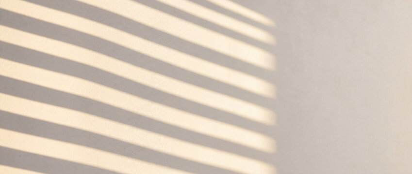 Sunlit diagonal blind shadows creating a minimal striped pattern on a beige interior wall