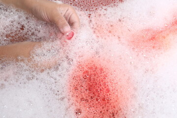Fototapeta premium Child holding a small pink toy in a bubble bath close-up.