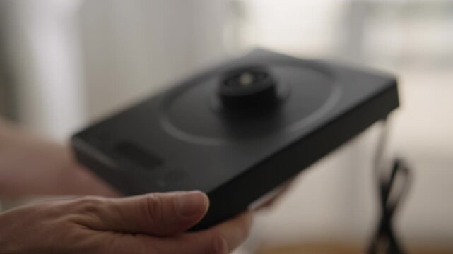 Detailed cropped shot of person hands holding and examining black electric kettle base, checking temperature controller and cleaning heating surface. Shooting in slow motion