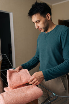 Man hanging freshly washed pink towels on indoor drying rack, engaged in everyday domestic tasks and taking responsibility for household laundry. Concept of housekeeping and cleaning.