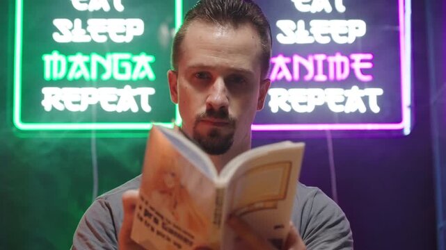 Man reading manga comic under two anime and manga neon signs 4K
