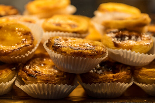 Primer plano de un mont&oacute;n de pasteles de Bel&eacute;n con su cl&aacute;sica superficie tostada sobre una bandeja. Dulces de crema tradicionales listos para la venta en una pasteler&iacute;a o cafeter&iacute;a.