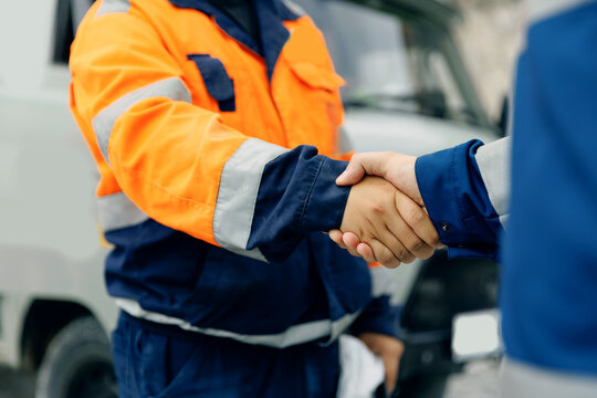 Industry workers shaking hands near work truck on roadside