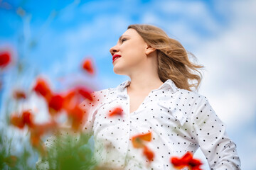 Low angle profile portrait of smiling elegant woman against blue sky with blurred red poppies. Summer bliss concept, peace of mind, aesthetic fashion portrait and confidence in nature. © 5ph