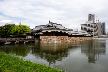 Naklejka premium Traditional main gate and stone walls of Hiroshima Castle reflected in the moat water, Japan