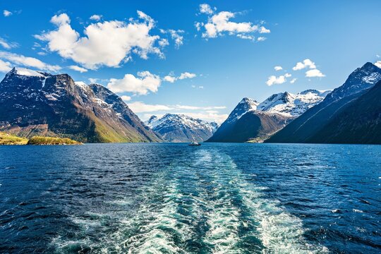 View from the stern of a ship toward the mountains at the horizon in a fjord in Norway with a boat in the middle