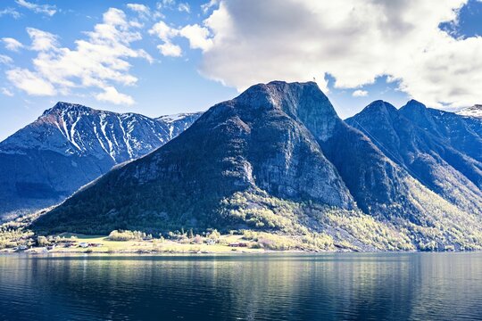 Mountains reflect in water while clouds hover above in Norway during sunny daylight