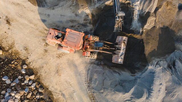 Aerial view of an orange wheel loader moving sand in the Babakan quarry with industrial machinery and piles of gravel Karanglewas, Central Java, Indonesia.
