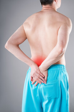 Lower back pain, sciatica or lumbago concept. Rear view of shirtless man holding his aching lumbar spine with red inflammation graphic