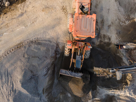 Aerial view of an orange wheel loader moving sand and gravel at the Babakan quarry site with a worker standing nearby in Karanglewas, Central Java, Indonesia.