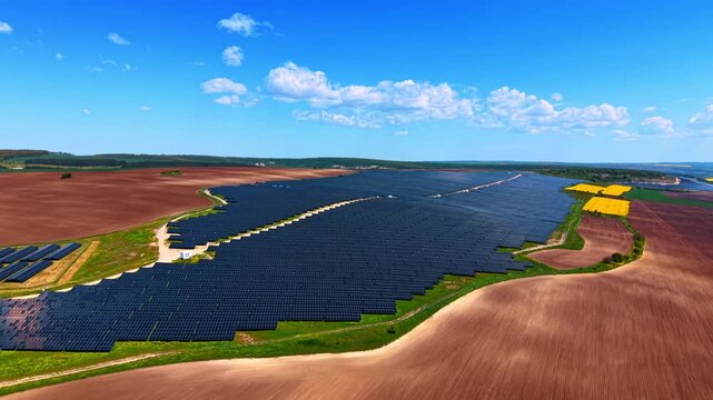 Panoramic aerial view of solar farm between plowed and rapeseed fields.
