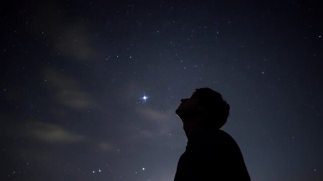 Man silhouetted looking up at bright star in clear night sky over rural landscape