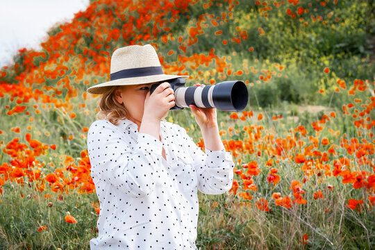 Woman photographer in straw hat taking pictures with large telephoto lens in poppy field. Creative outdoor profession, digital content creation, photography gear and workspace concept.