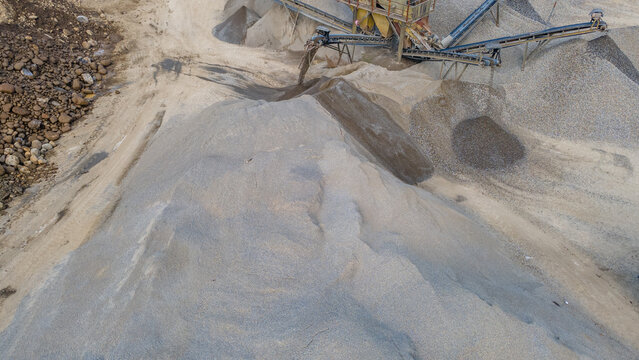 Aerial view of a sand and gravel quarry with large aggregate mounds and industrial conveyor belts in Karanglewas, Central Java, Indonesia.