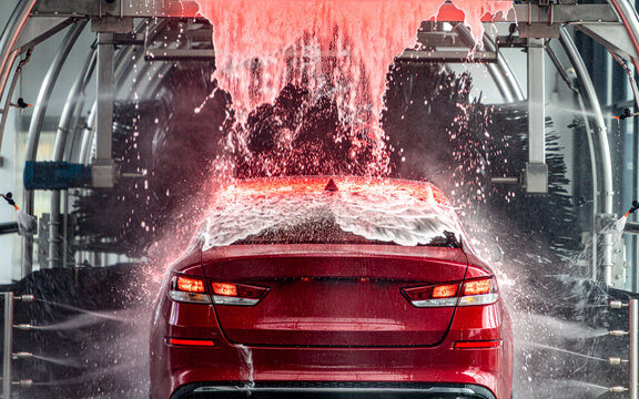 Red car in red foam in automatic tunnel car wash. 
