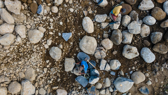 Aerial view of workers manually breaking large river stones and boulders with hammers in a quarry near Babakan, Karanglewas, Central Java, Indonesia.