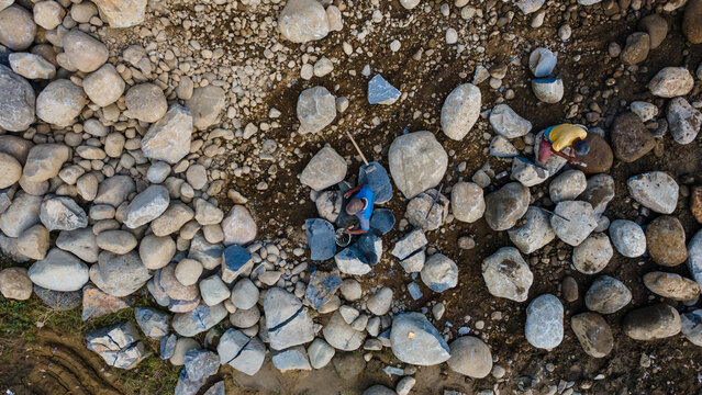 Aerial view of workers breaking large river stones and boulders with tools on the rocky ground in Karanglewas, Central Java, Indonesia.